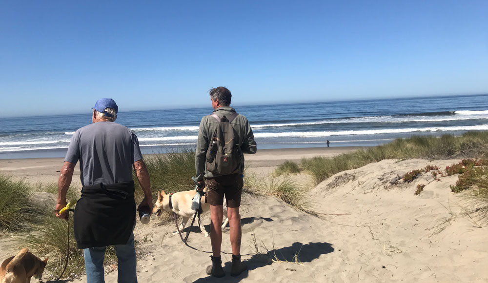 Two men walking in sand dunes near the ocean