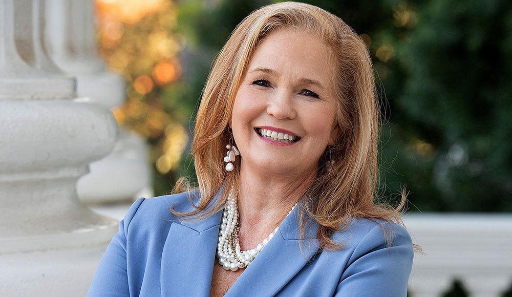 Blond woman wearing a jacket and pearls, photographed outdoors