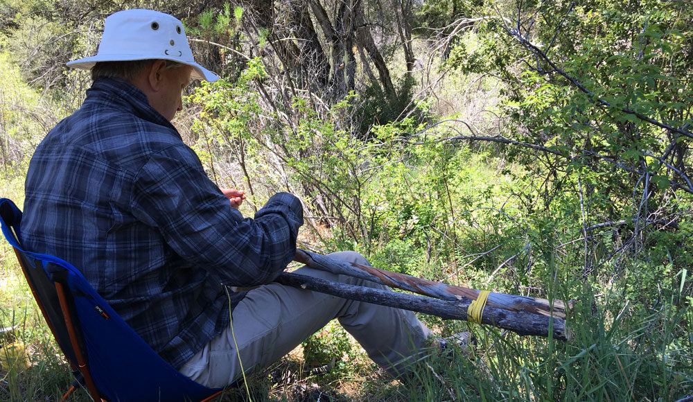 Man making a crutch while sitting in the wilderness