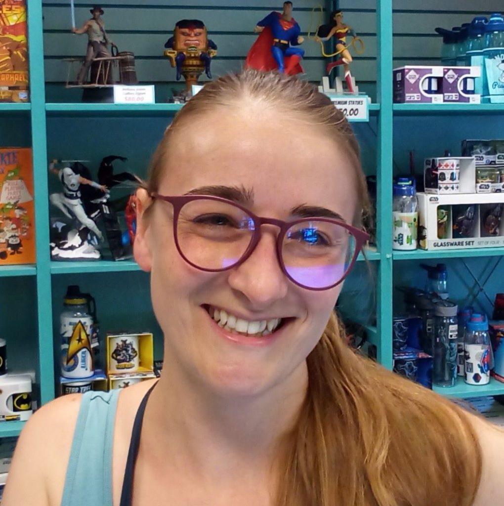 36 year old Trisha Wolfe with shelves of fantasy toys behind