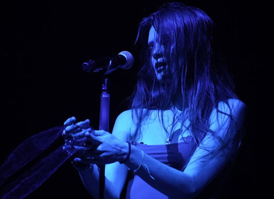 Woman singing into a microphone under a blue spotlight