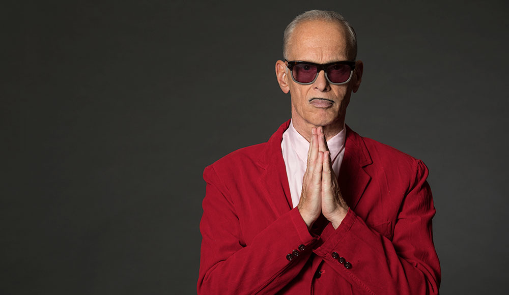 Photo of man in a red suit wearing sunglasses and holding his hands as if praying