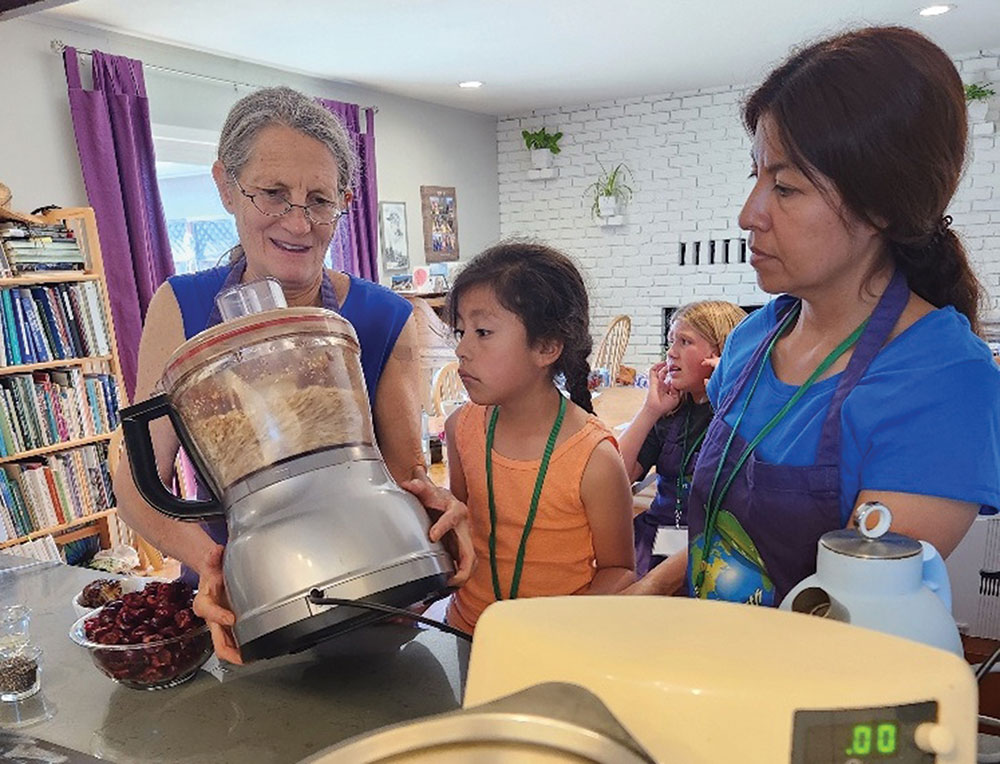 Woman holding a food processor in a classroom next to a girl and another adult