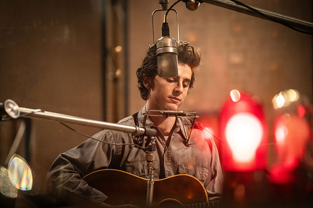 Man playing guitar and harmonica in front of a microphone