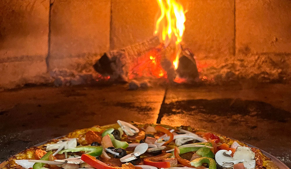 Pizza in front of the opening into a wood-fired stove