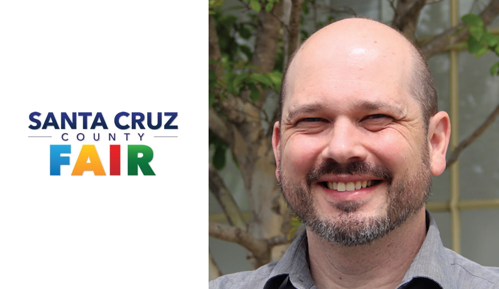 Man next to a logo of the Santa Cruz County Fair