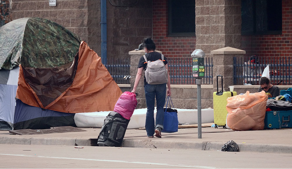 Woman with luggage walking through a homeless encampment on a city street